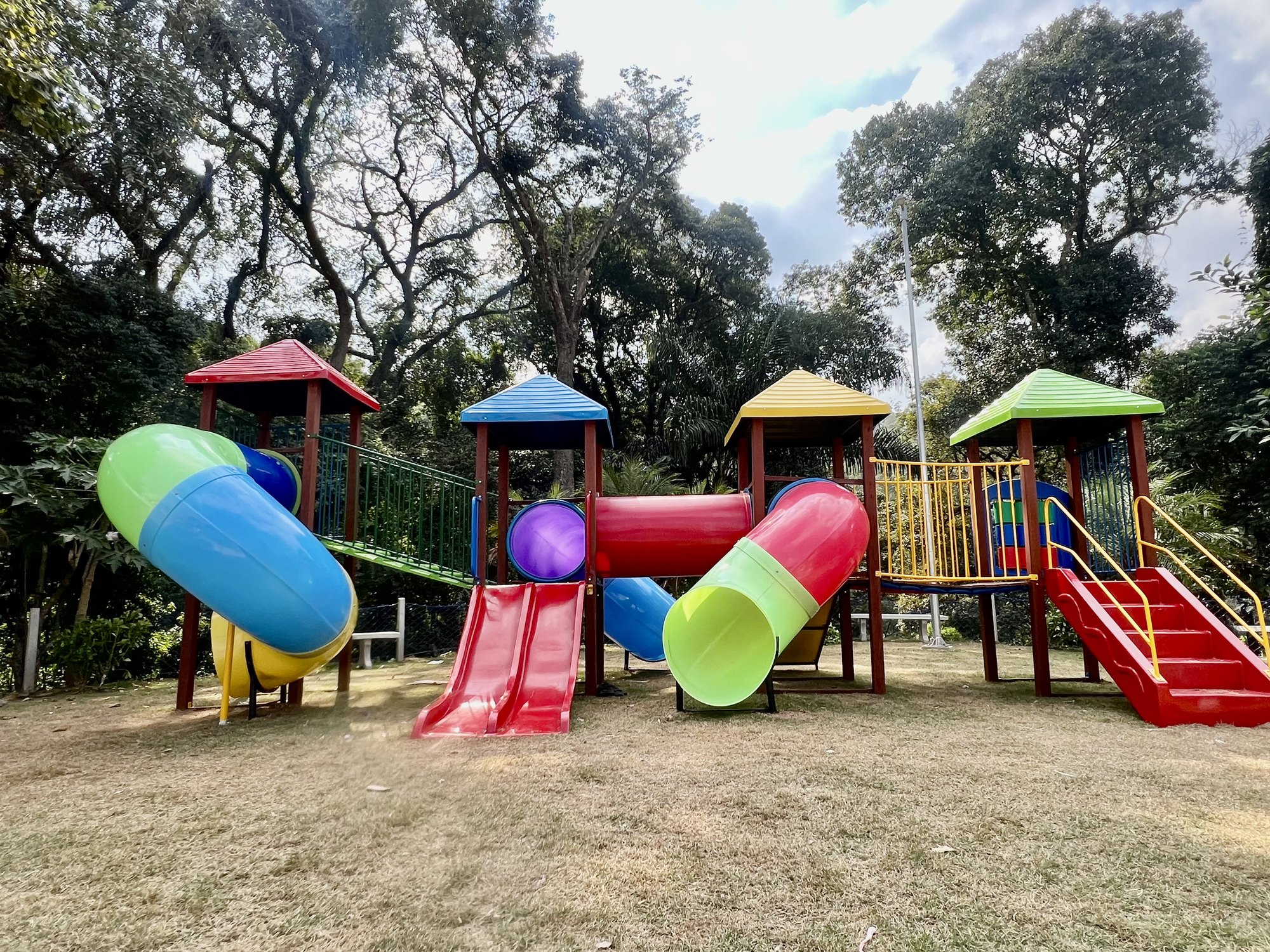 Playground com tubos coloridos instalado em área externa arborizada, fabricado pela Upa Upa