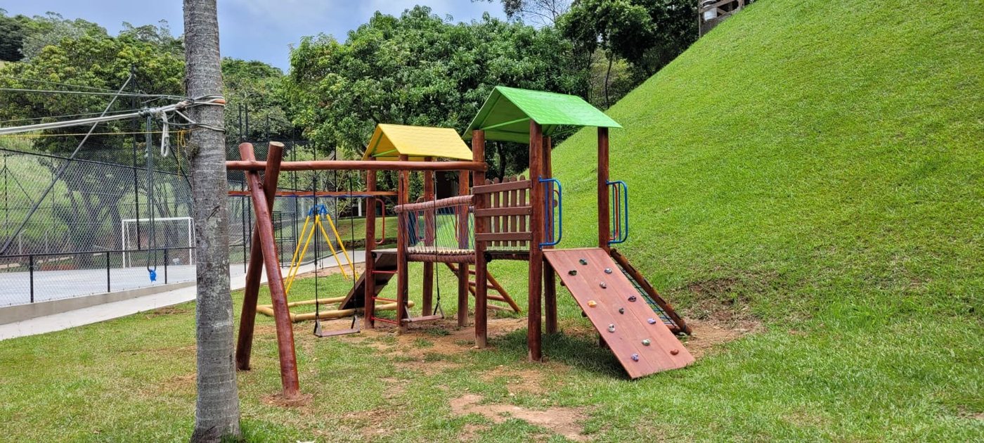 Playground de madeira de eucalipto em área gramada, com rampa de escalada e balanços