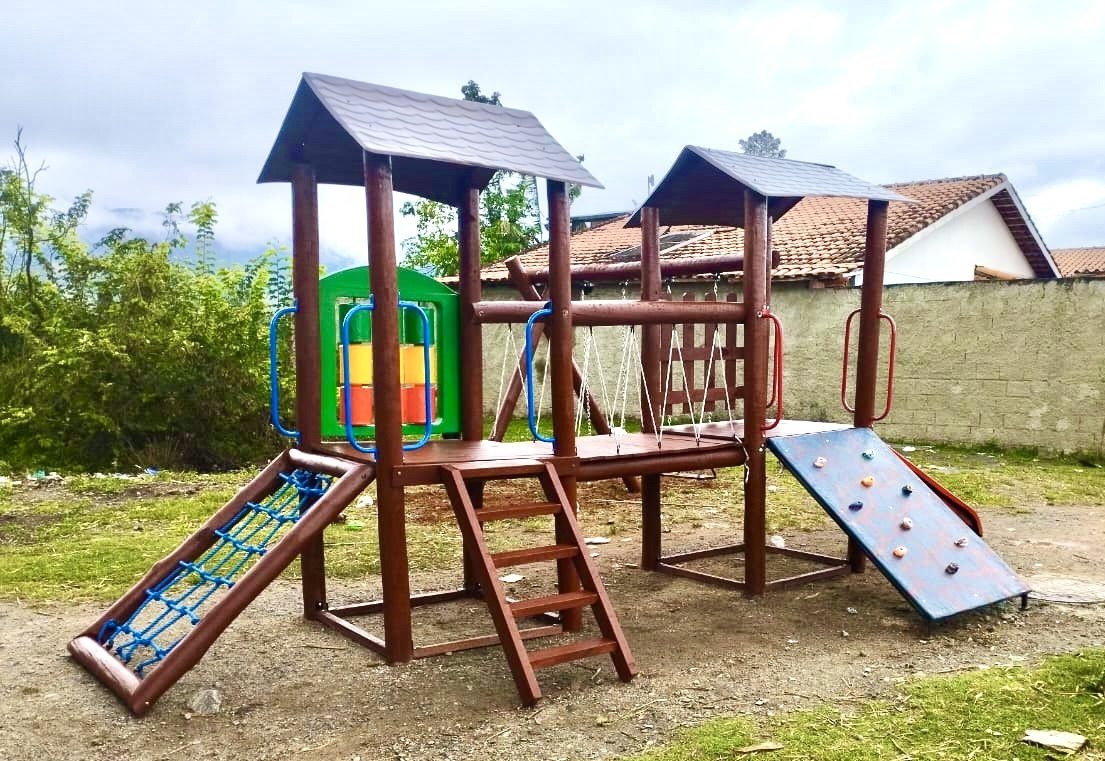 Playground de madeira de eucalipto com duas torres cobertas, rampa de rede, parede de escalada e balanços