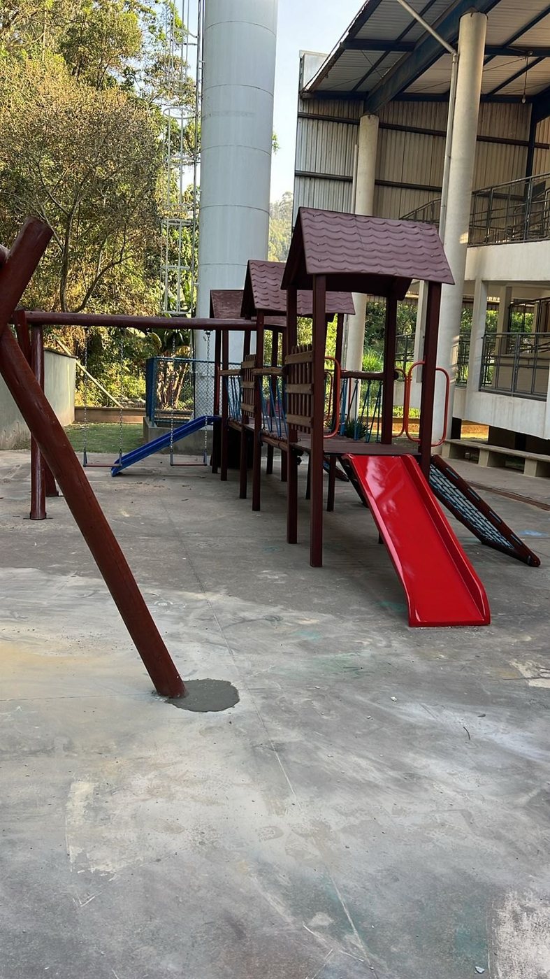 Playground de madeira de eucalipto instalado em pátio coberto, com escorregador e balanços